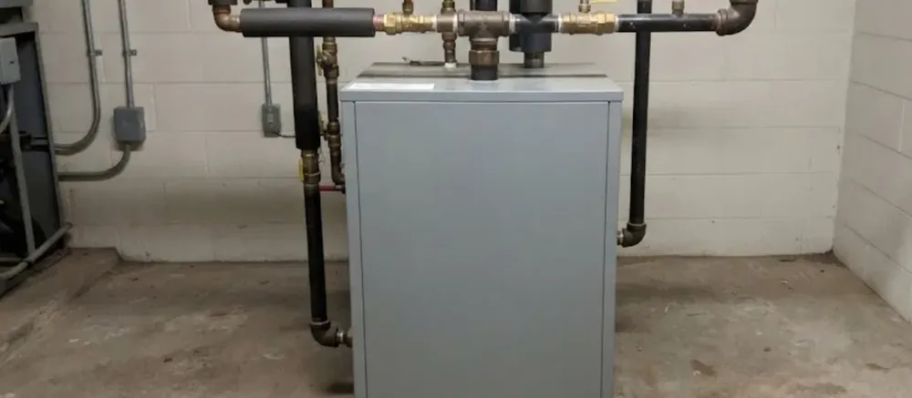 Boiler with pressure gauge and black iron piping in a basement utility room
