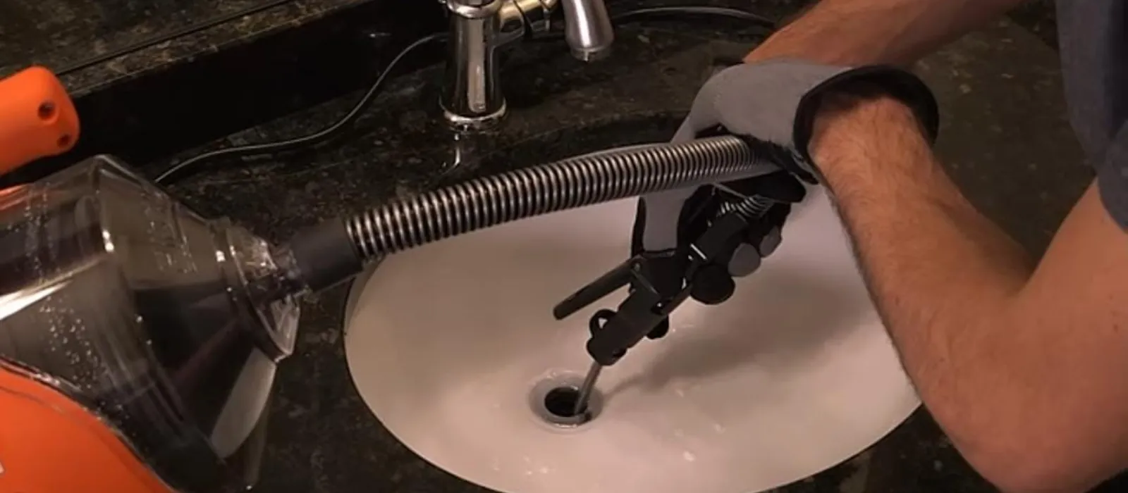 Drain cleaning machine cable being fed into a bathroom sink drain