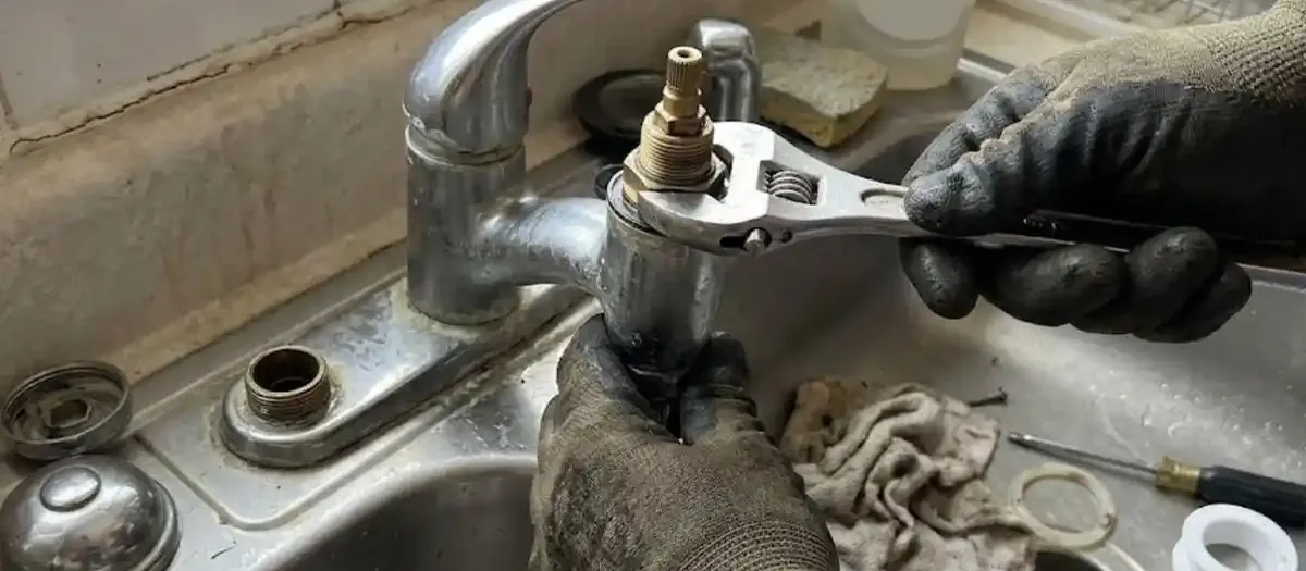 Gloved hands using a wrench on a kitchen faucet base