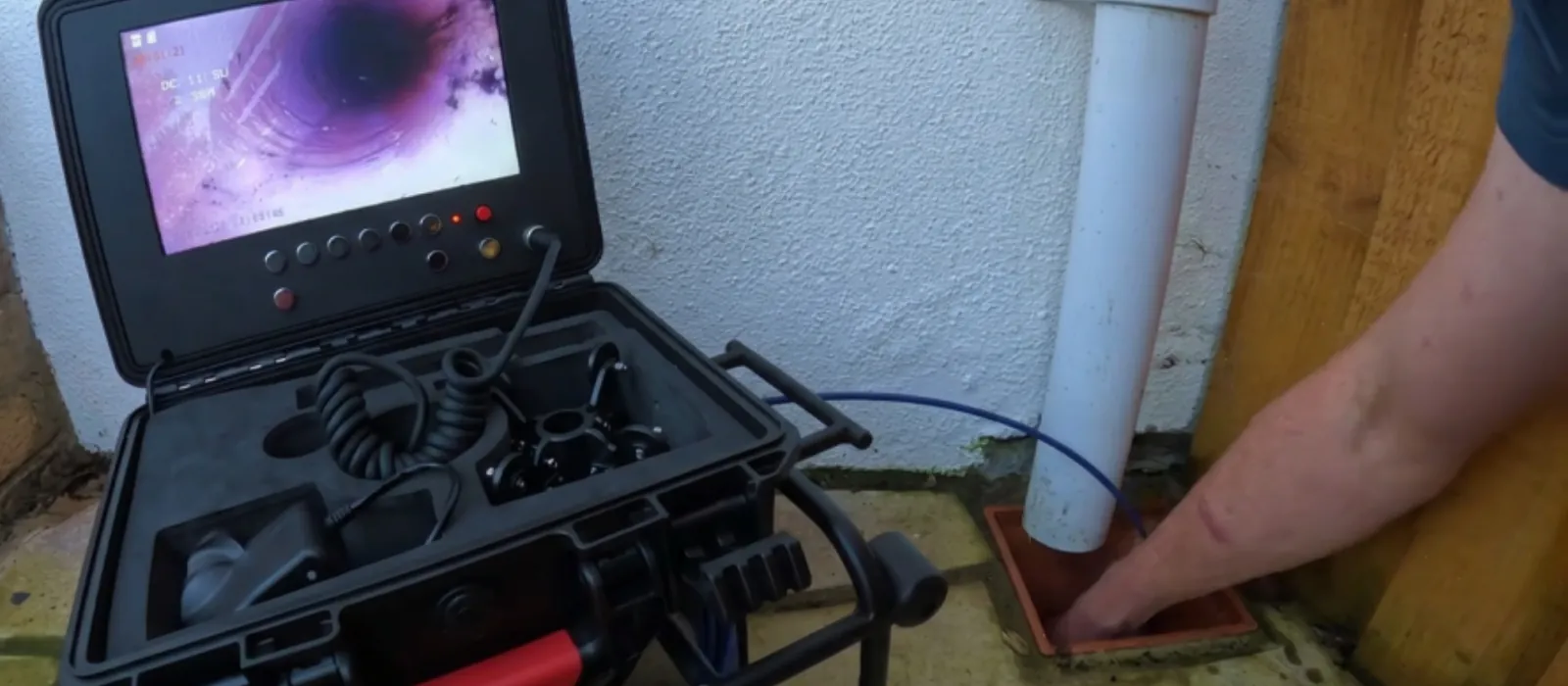 Sewer camera monitor in a hard case beside a cleanout pipe