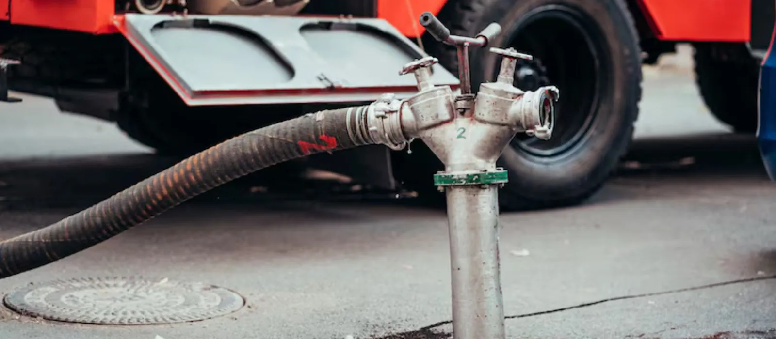 Service truck hose connected to a sewer access point in a street